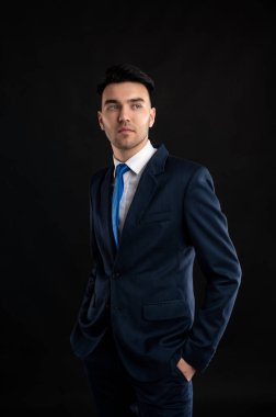 Siyah arka planda mavi takım elbiseli ve kravatlı bir iş adamı portresi