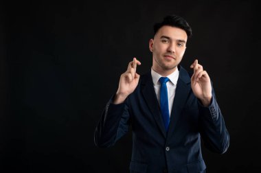 Mavi takım elbiseli ve kravatlı bir iş adamının portresi siyah arka planda izole edilmiş ve fotokopi alanı reklam alanında çift parmak gösteriyor.