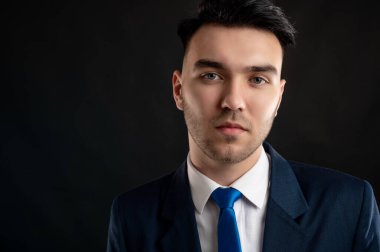 Mavi takım elbiseli ve kravatlı bir iş adamının yakın plan portresi fotokopi alanındaki siyah arka planda izole edilmiş.