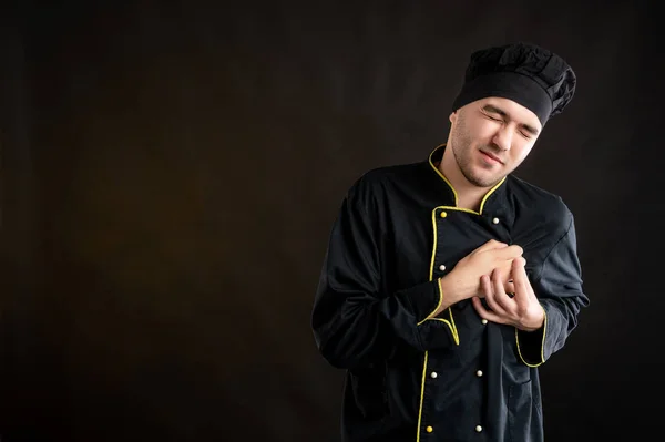 Portrait of young male dressed in a black chef suit suffering heart ache or breast pain, cardiac problems posing on a brown backround with copy space advertising area