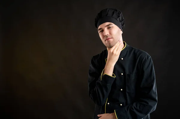 Portrait of young male dressed in a black chef suit with open arms looking up, sore throat posing on a brown background with copy space advertising area