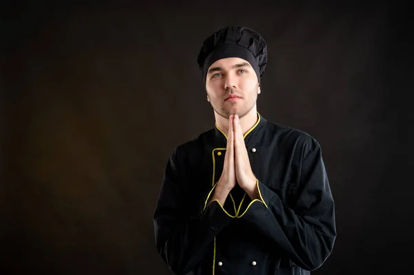 Portrait of young male dressed in a black chef suit is praying posing on a brown background with copy space advertising area