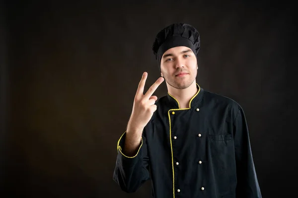 身穿黑色厨师西服的年轻男性画像 用手指在褐色背景上摆出两个手指 并有一个复制空间广告区 — 图库照片