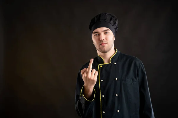 Portrait of young male dressed in a black chef suit showing fuck you posing on a brown background with copy space advertising area