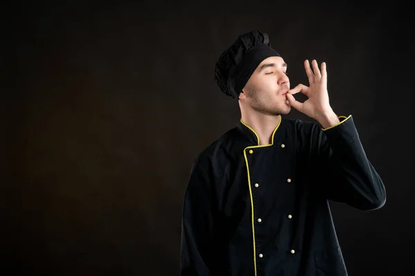 Portrait of young male dressed in a black chef suit showing OK sign posing on a brown background with copy space advertising area