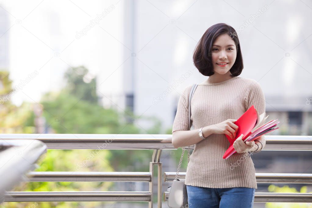 Beautiful Asian female college student holding her books smiling happily standing outdoor, people education learning high school program smart teenager concept
