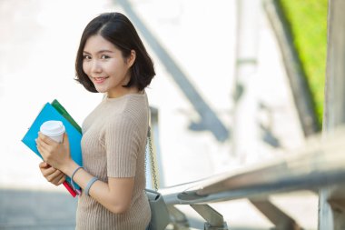 Güzel Asyalı kadın üniversite öğrencisi kitaplarını ve bir fincan kahve ayakta açık, insanlar eğitim yüksek okulu programı akıllı genç kavramı öğrenme holding