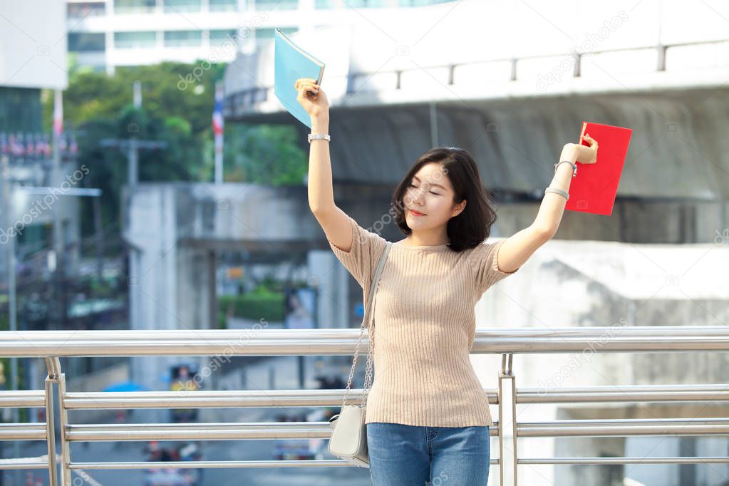 Beautiful Asian female college student holding her books smiling happily standing outdoor, people education learning high school program smart teenager concept