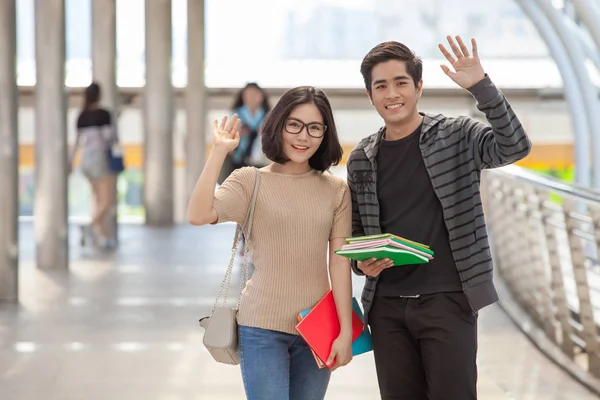 Man and woman students holding many books waving hands say hello to their friends