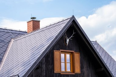 Yenilenmiş bir orman kulübesinin cephesi boynuzları ve açık bir penceresi ve gökyüzü olan bir bacası ile korunuyor.
