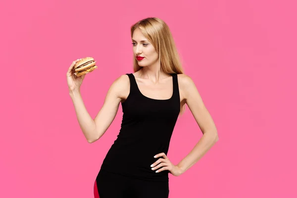 ピンクの背景の美しい少女は ハンバーガーを保持しています 不健康な食事の概念 — ストック写真