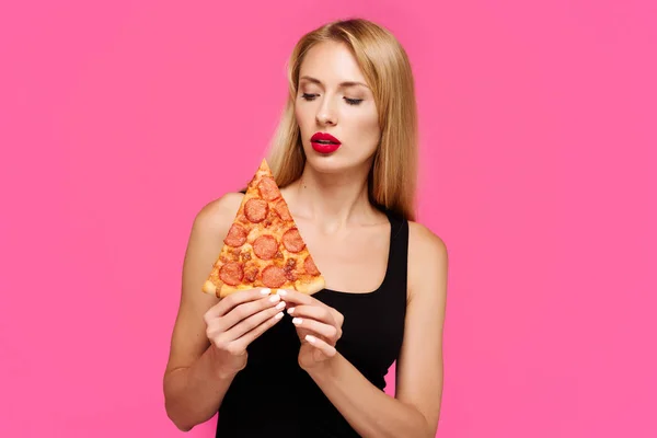 Young slender girl with a pink background holds a pizza in her hands. Concept of unhealthy fat junk food