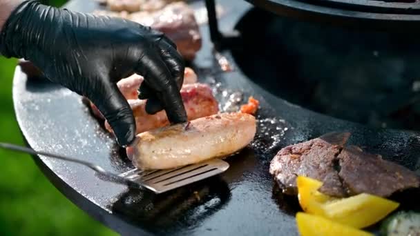 Cocine en guantes de nitrilo negro da vuelta las salchichas en una barbacoa, un aperitivo para la cena — Vídeos de Stock