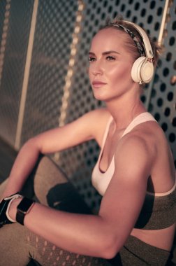 Duvarın önündeki kulaklıklı kadın portresi. Formda kız antrenmandan sonra mola veriyor.