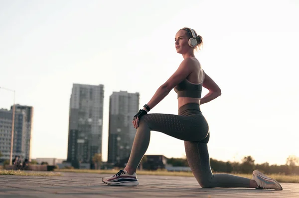 Junge Läuferin Fitnessbekleidung Und Kopfhörer Macht Dehnübungen Freien Beleuchteter Sonnenuntergang — Stockfoto