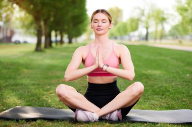Spor salonundaki kadın meditasyon yapıyor ve yoga pozisyonunda dinleniyor. Parkta loto pozisyonunda yoga yapan bir kız.