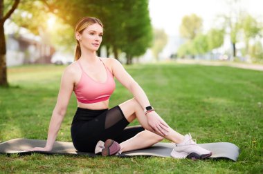 Omurgası bükülmüş bir kadın. Yoga yapan kız, balıkların yarı lordu Ardha Matsyendrasana, şehir parkında poz veriyor.