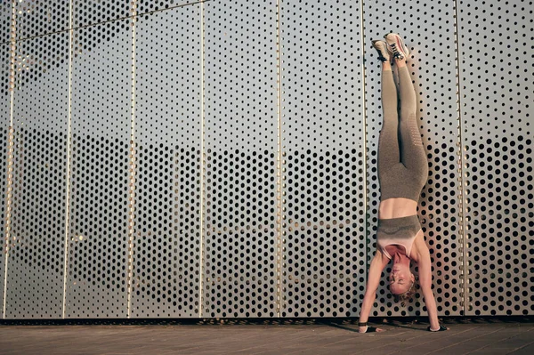 Fittes Mädchen in Sportbekleidung, das kopfüber vor einer Wand im Freien steht. Starke muskulöse Frau bei körperlicher Anstrengung. — Stockfoto