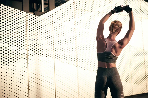 Kaslı güçlü vücudu olan arka görüş atleti bir kadın. Formda kız, gri duvarın önünde esneme egzersizi yapıyor.