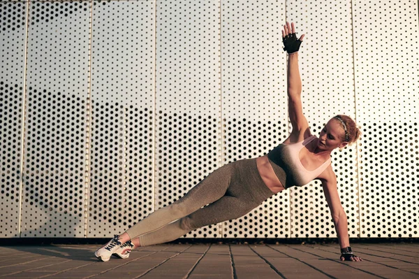 Fit strong woman standing in Side Plank pose, Vasisthasana while practicing yoga outdoors, in city. Healthy lifestyle and relaxation concept