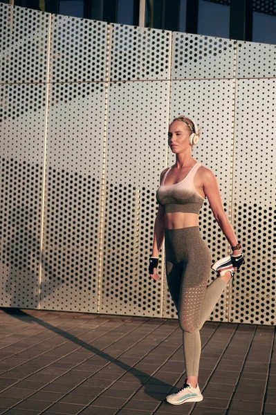 Fit muskulöse sportliche Frau macht Dehnübungen vor der Wand im Freien. Starkes Mädchen wärmt sich beim Joggen auf und hört Musik über Kopfhörer — Stockfoto
