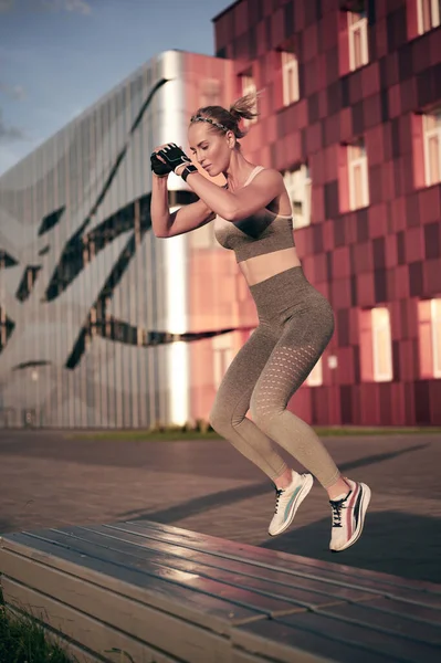 Fit Frau in Sportbekleidung springt auf Bank im Freien. Gesunder Lebensstil, Motivationskonzept. — Stockfoto