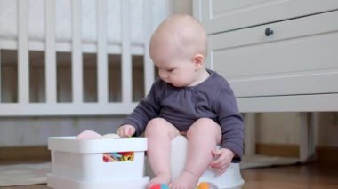 Yeni doğmuş bebek lazımlıkta oturuyor ve oyuncaklarla oynuyor.