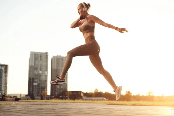 Fitness-Frau beim Springen in Sportbekleidung und beim Musikhören über Kopfhörer. Sportliches Mädchen, körperliche Aktivität, Motivationskonzept — Stockfoto