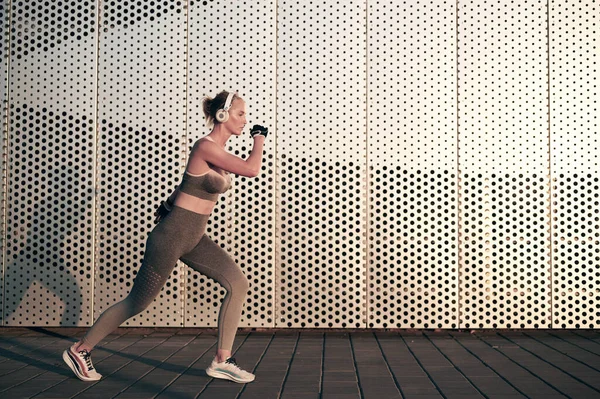 Fitte sportliche Frau beim Joggen im Freien. Gesunde junge Sportlerin beim Fitnesstraining und Musikhören im Kopfhörer vor der Wand — Stockfoto