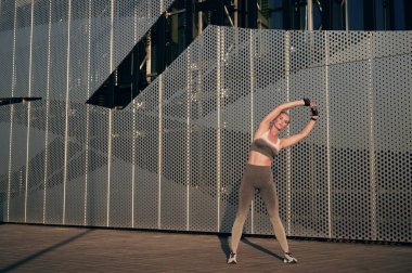 Genç beyaz kadın yaz parkında binanın önünde koştuktan sonra fiziksel egzersiz yapıyor. Sağlıklı yaşam tarzı, spor anlayışı