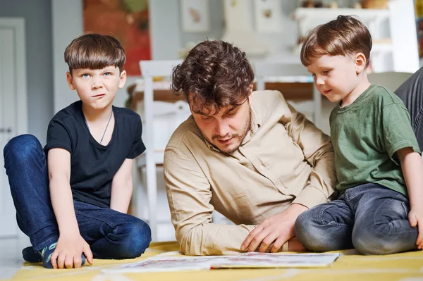 Père avec des fils lisant le livre, passant du temps ensemble à la maison et couché sur le sol — Photo