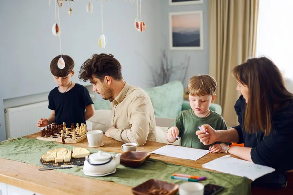 Famille heureuse passer du temps ensemble à la maison, père jouer aux échecs avec fils, mère dessiner avec enfant à la maison — Photo