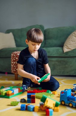 Anaokulu beyaz çocuğu yerde müteahhitle oynuyor, bir sürü renkli plastik blok yapıcısı var.