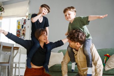 Küçük oğulları olan mutlu bir aile evde eğleniyor. Gülümseyen ebeveynler ve anaokulu çocukları birlikte eğleniyorlar, aile boş vakitlerin tadını çıkarıyor.