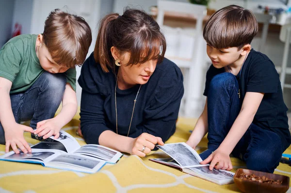 Młoda biała matka spędza czas w domu z synami i czyta książki na podłodze. Szczęśliwy rodzic bawiący się z przedszkolakami. Koncepcja edukacji domowej — Zdjęcie stockowe