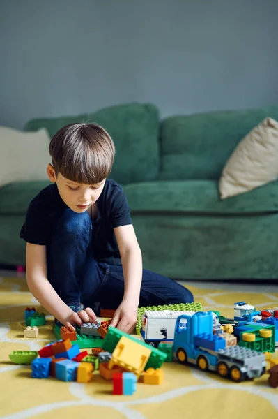 Preescolar chico caucásico jugando con el constructor sentado en el suelo, un montón de bloques de plástico colorido constructor — Foto de Stock