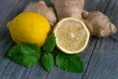 Taze zencefil kökü ve limon ve nane veya eski gri ahşap arka planda mellis yaprakları.