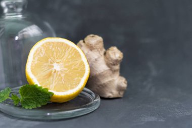 Taze zencefil kökü ve limon ve nane ya da mellis yaprakları şeffaf cam bir zil altında gri heterojen bir zemin üzerinde