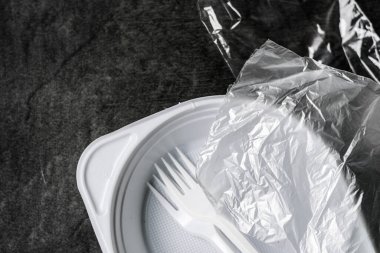 Gri-siyah arka planda beyaz plastik çatallar, plakalar ve paketler. Plastik atık. Çevresel konsept. Tek kullanımlık plastiği yasakla. Gezegenin çevre kirliliği ve ekolojisi
