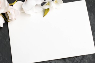 Etrafta narin beyaz çiçekler ve güller var. Gri arkaplandaki yazıtlar için beyaz sayfa, kopyalanmış boşluk