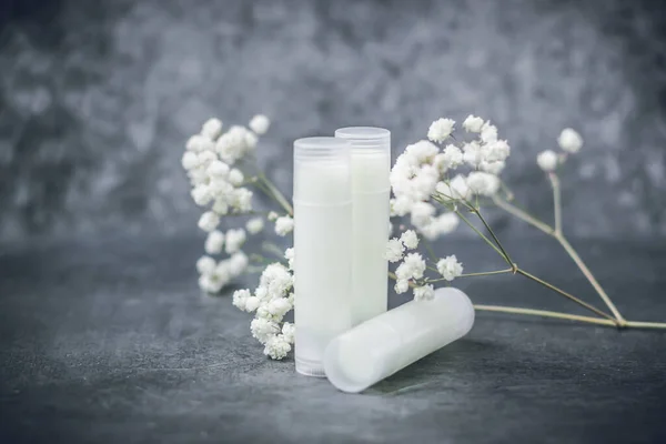 lip balm with flowers in a transparent tube with white contents. DIY lipstick made from natural eco-friendly ingredients. hand made on a gray background