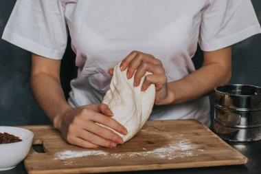 Genç kız hamuru gri arka planda doğal manikürlü uzun tırnaklı beyaz bir tişörtle yoğuruyor. Yemek yaparken kuru üzümlü hamur.