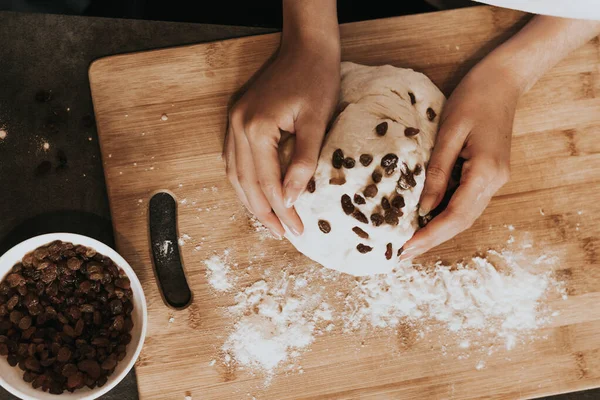 Young figured girl kneads the dough in a white T-shirt with long nails with natural manicure on a gray background. Lush dough with raisins during cooking