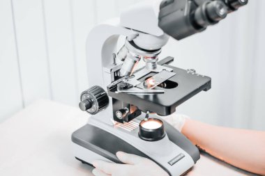 Bir veteriner laboratuarındaki mikroskobun yakın çekimi. Gripullu tıbbi araştırma virüs merkezi. Göz mercekleri yakında, biyomateryaller inceleniyor ve iş yerinde aydınlanma var. Kadın bir laboratuar asistanı.