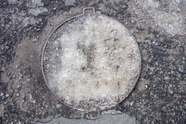Asfalt kaplı metal kapaklı rögar deliği.