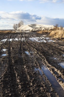 Çamur ve su birikintileri içinde belgili tanımlık geçmiş kum tepeleri ile toprak yol üzerinde.