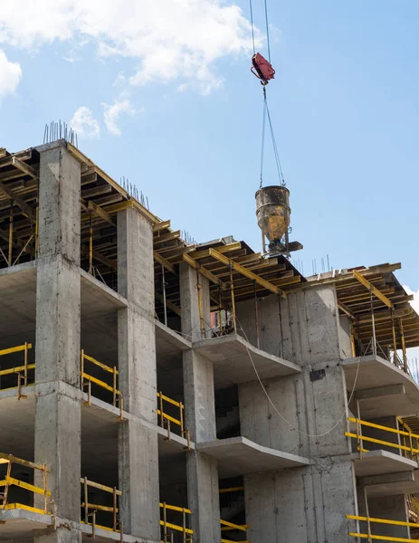 Concrete skip on the tower crane's hook over the framework of the future building