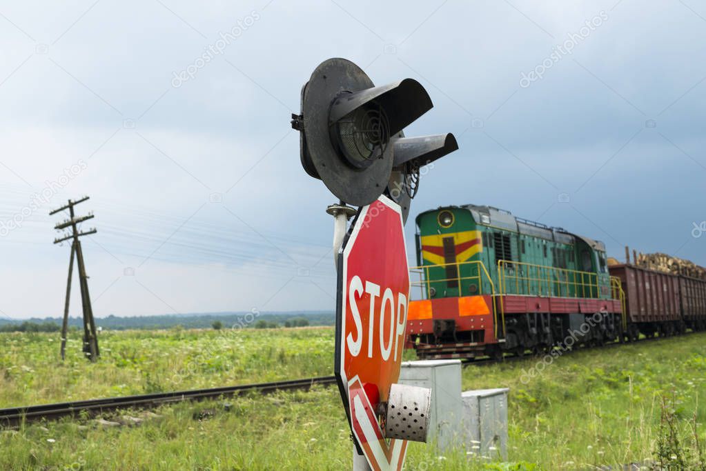 Traffic lights and signs at the railroad crossing and the approaching freight train (Ukraine).