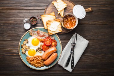 Tam İngiliz kahvaltısı ile kızarmış yumurta, sosis, pastırma, fasulye, mantar, domates ekmek tost tereyağı ile bir plaka üzerinde. Geleneksel İngiliz yemek, üstten görünüm, rustik ahşap adam