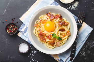 Geleneksel İtalyan makarna yemeği, yumurtalı spagetti carbonara, parmesan peyniri, siyah taştan arka planda pastırma, üst manzara. İtalyan yemeği ve makarna. 